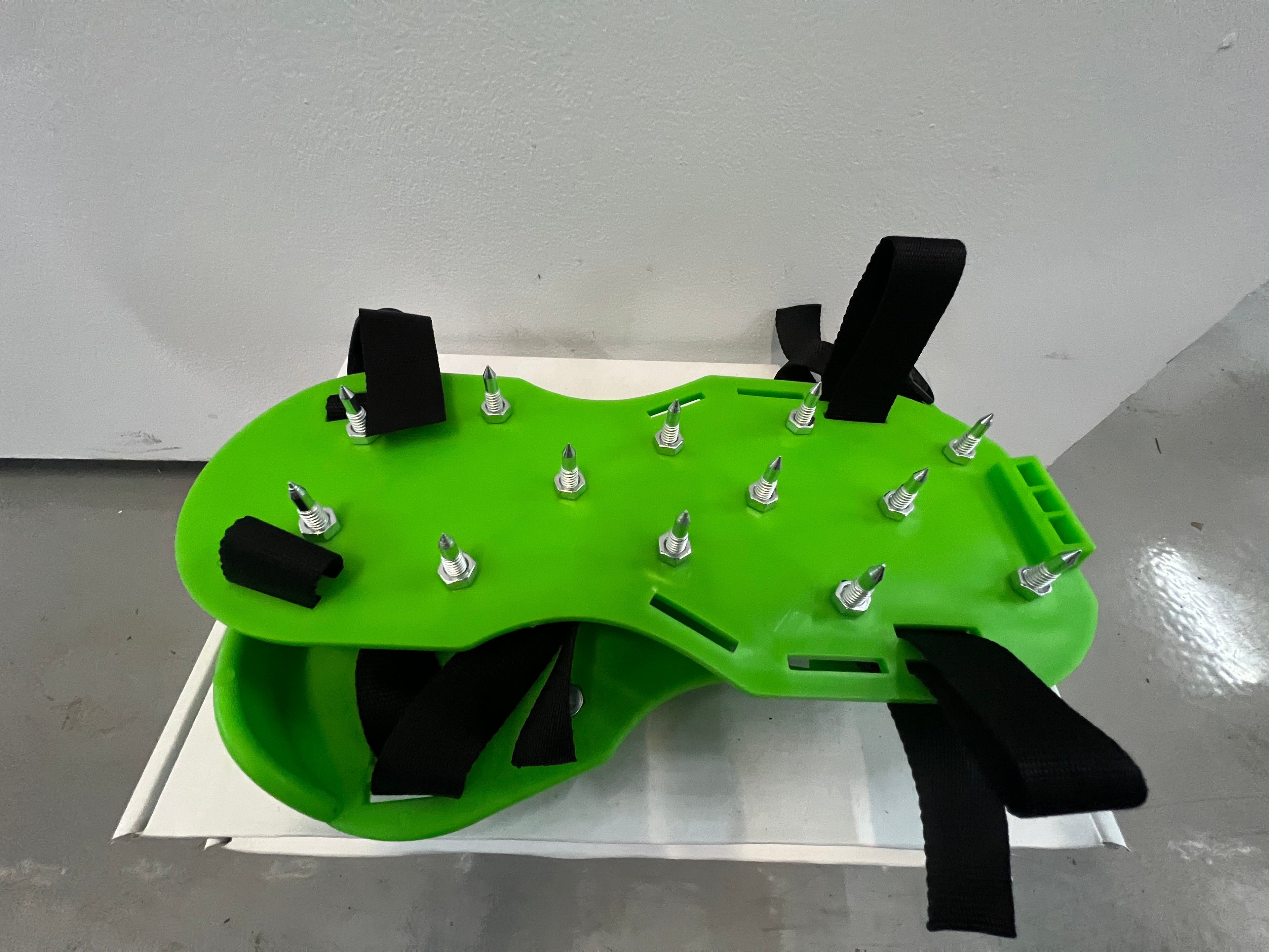 A pair of green spiked shoes with black straps designed for painting floors.
